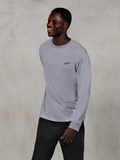Alpinestars Essentials Ageless LS Tee, långärmad t-shirt, silver, liten svart logotyp på bröstet, bärs av en leende modell med mörka byxor, avslappnad modern passform, vardagliga motorsport-livsstilskläder