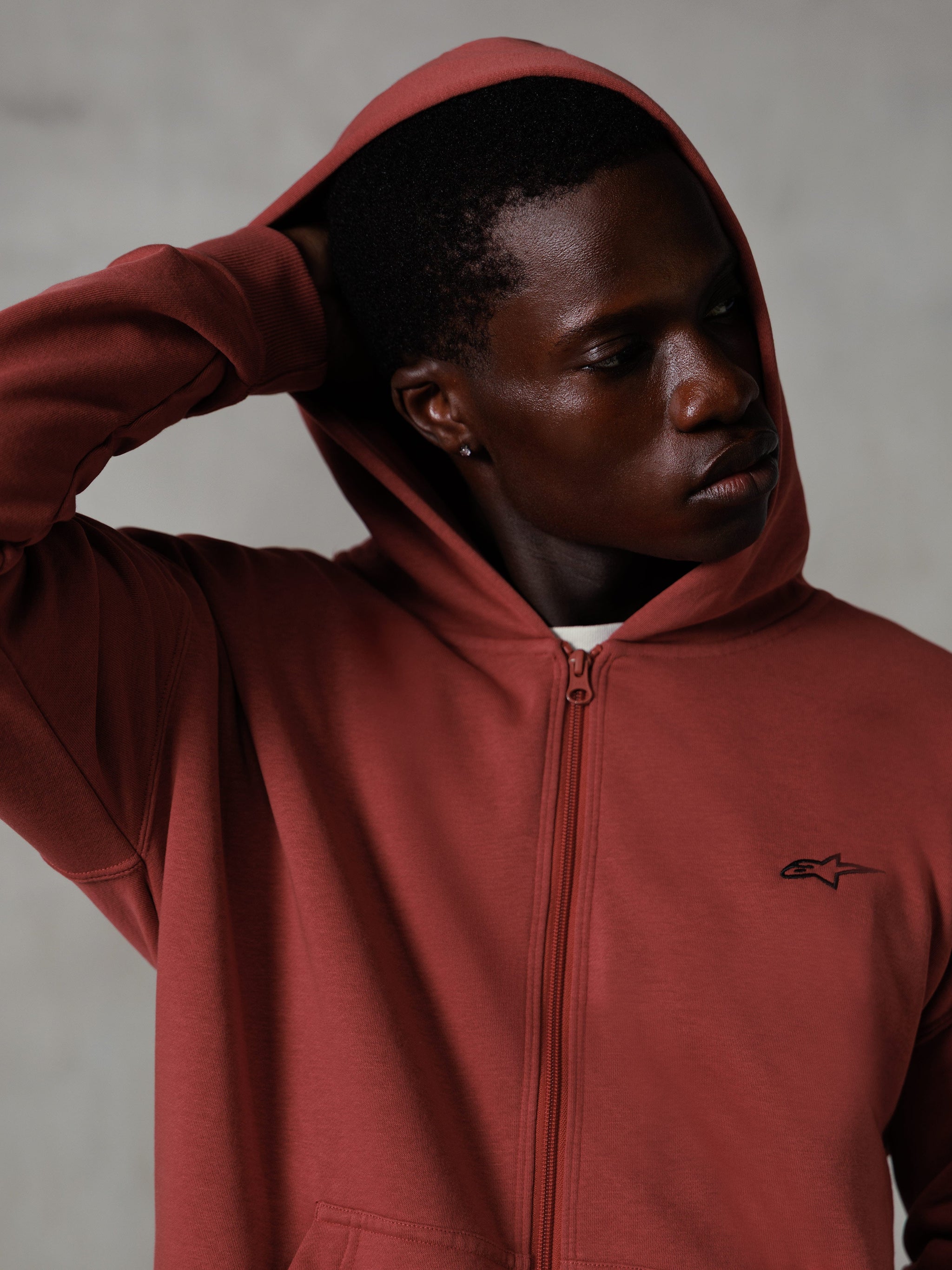 Alpinestars Essentials Ageless Zip Hoodie, tegelröd, casual lifestyle streetwear, huvan uppe med handen bakom huvudet, liten svart Astars-logotyp på bröstet, huvtröja i fleece med avslappnad passform