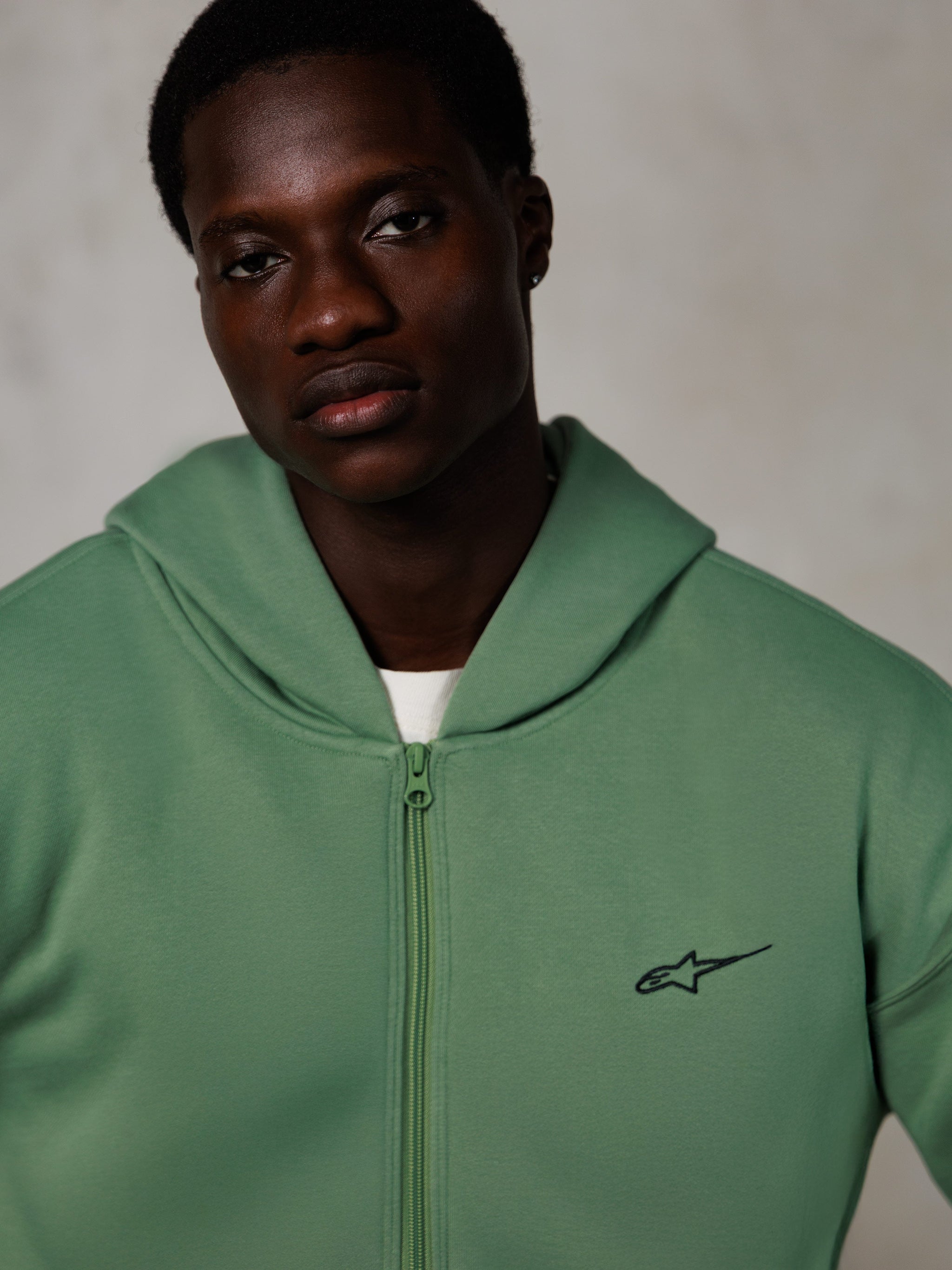 Alpinestars Essentials Ageless Zip Hoodie, lifestyle portrait, cactus green with small black logo, zip-up front, soft fleece texture, casual motorsport-inspired streetwear