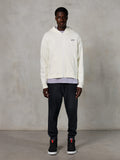 Alpinestars Essentials Ageless Zip Hoodie, vardaglig streetwear, off-white med en subtil svart logotyp på bröstet, hellång dragkedja fram, design med huva, avslappnad passform, stylad med svarta mjukisbyxor och sneakers