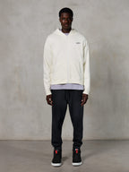 Alpinestars Essentials Ageless Zip Hoodie, vardaglig streetwear, off-white med en subtil svart logotyp på bröstet, hellång dragkedja fram, design med huva, avslappnad passform, stylad med svarta mjukisbyxor och sneakers