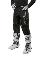 Alpinestars 2024 Fluid Graphite Pants, Motocross Pants, Gray and Black, worn with white and black motocross boots and gloves, featuring a large silver Alpinestars logo on the thigh, athletic sport fit for off-road riding