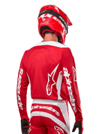 Motocrossförare iklädd Alpinestars 2024 Fluid Lurv Jersey, Mars Red och vit, vy bakifrån som visar vit Alpinestars-logotyp på ryggen och branding på ärmarna, matchad med röd hjälm och svarta handskar, professionell utrustning för terrängkörning