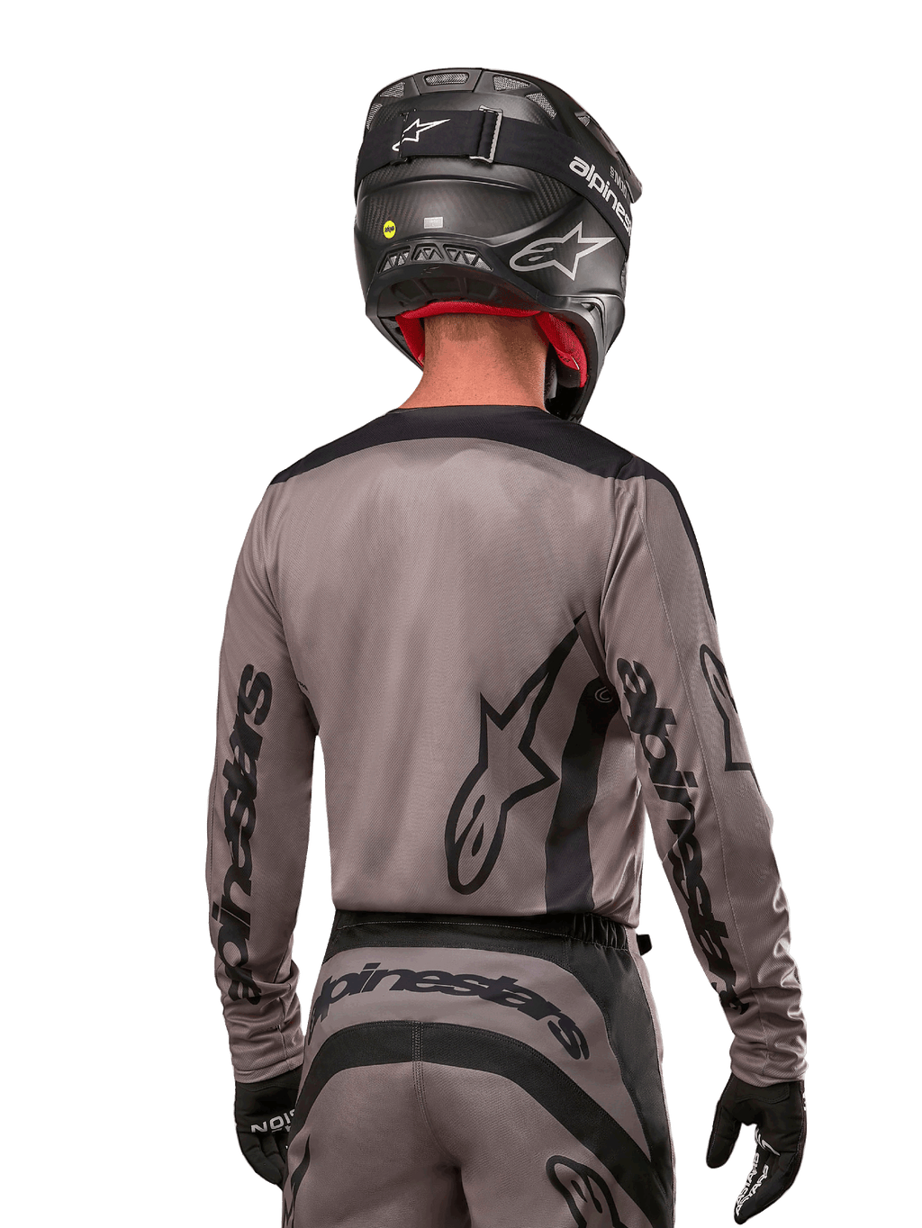 Motocrossförare sedd bakifrån i Alpinestars 2024 Fluid Lurv Jersey i Mud Black, med svart Alpinestars-logotyp på ärmar och rygg, matchad med svart hjälm och tillhörande utrustning för terrängkörning