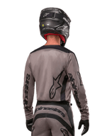 Motocrossförare sedd bakifrån i Alpinestars 2024 Fluid Lurv Jersey i Mud Black, med svart Alpinestars-logotyp på ärmar och rygg, matchad med svart hjälm och tillhörande utrustning för terrängkörning