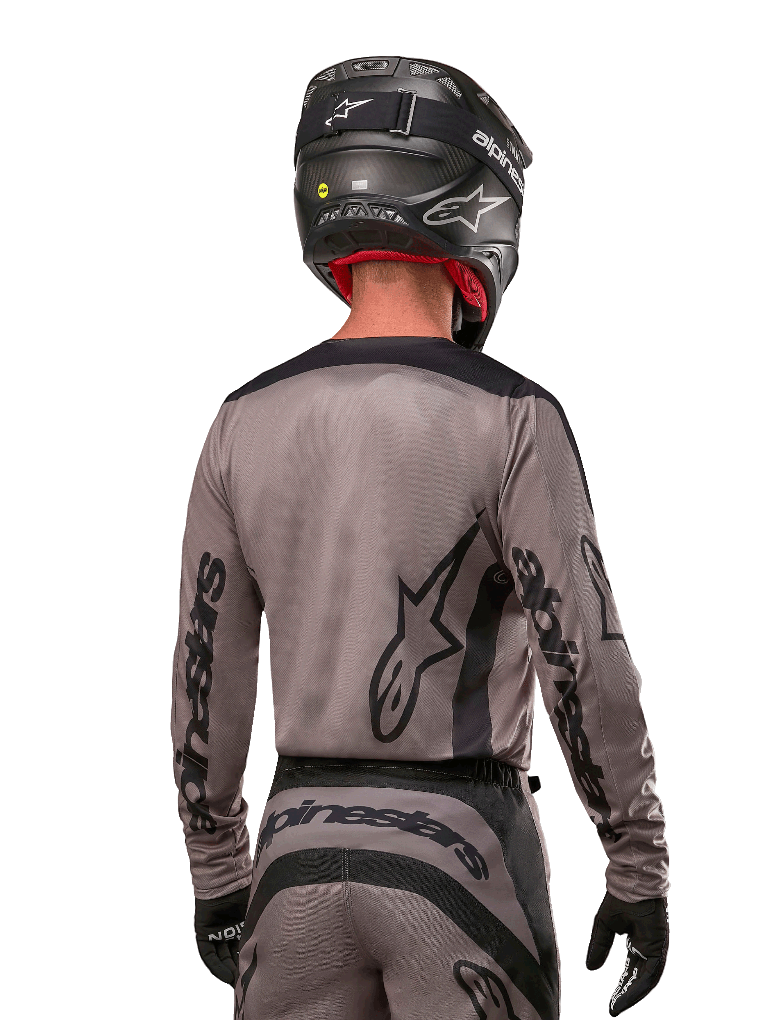Motocrossförare sedd bakifrån i Alpinestars 2024 Fluid Lurv Jersey i Mud Black, med svart Alpinestars-logotyp på ärmar och rygg, matchad med svart hjälm och tillhörande utrustning för terrängkörning