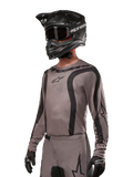 Alpinestars 2024 Fluid Lurv-tröja, motocrosströja, grå och svart, långärmad design med svängda svarta ränder och logotyper, bärs med matchande byxor och en svart motocrosshjälm, koordinerad racingutrustning för terrängkörning