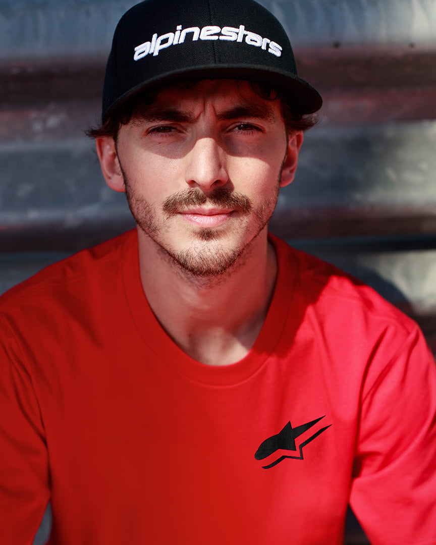 Alpinestars Formulate Csf T-shirt i rött, Francesco Bagnaia bär en kortärmad t-shirt med svart Astars-logotyp och svart baseballkeps, casual motorsport streetwear