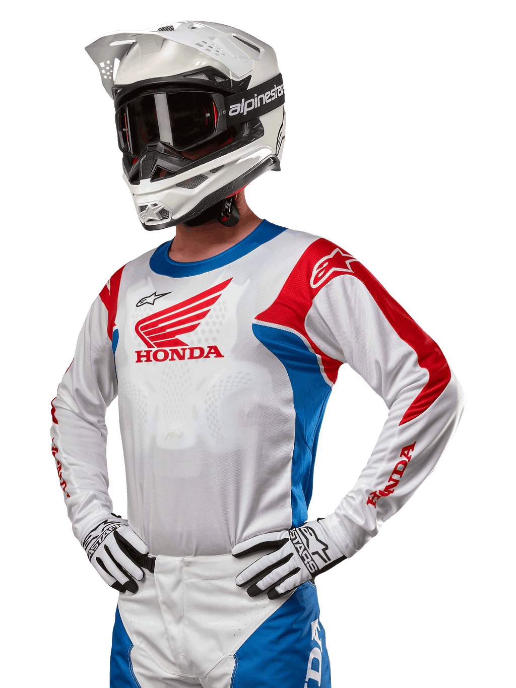 Motocrossförare i Honda Racer Iconic-tröja i vitt, klarblått och klarrött, med en stor Honda-vinglogotyp på bröstet, vit Alpinestars-hjälm och matchande vita och svarta handskar, koordinerad utrustning för offroad-prestanda