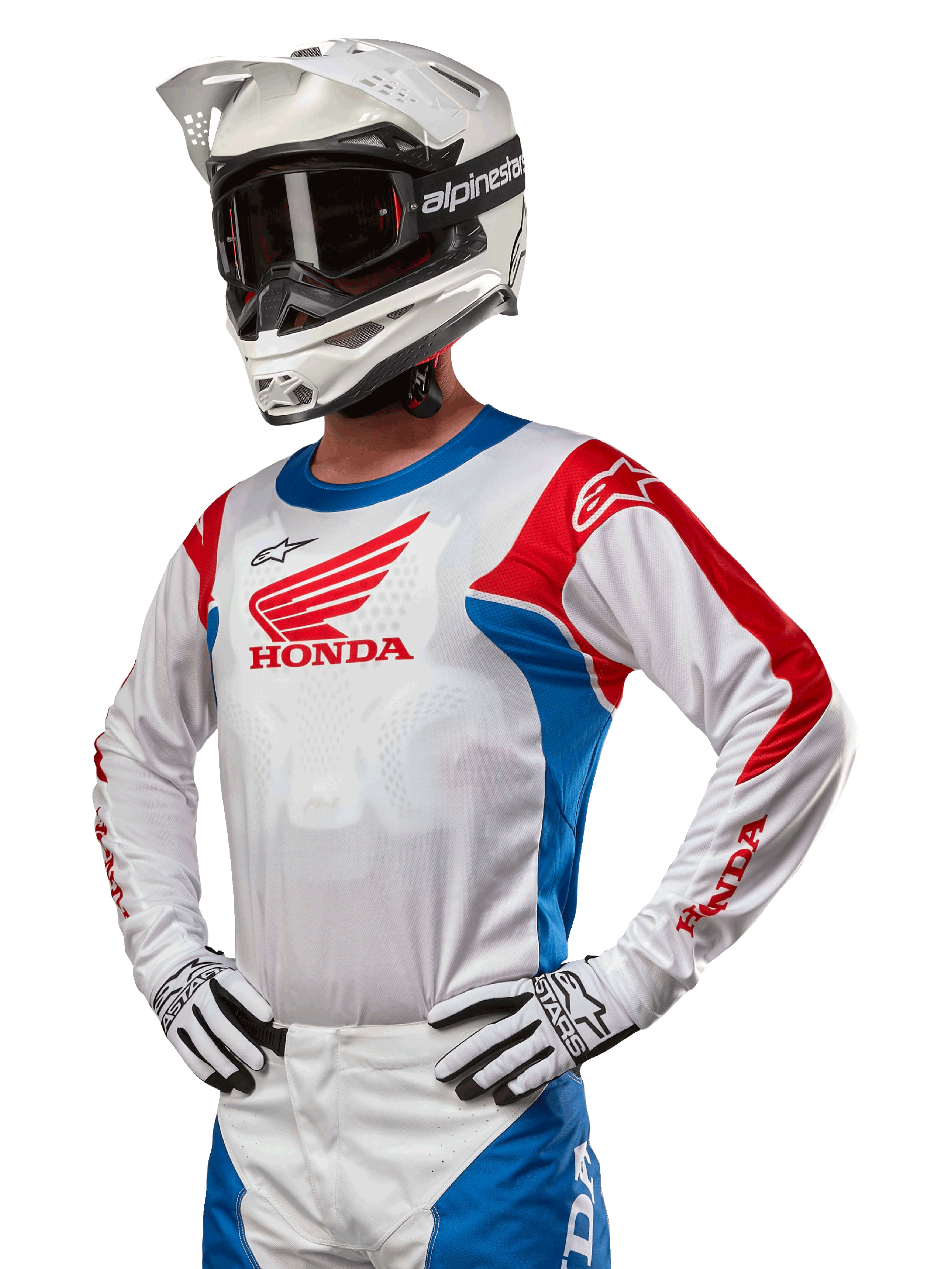 Motocrossförare i Honda Racer Iconic-tröja i vitt, klarblått och klarrött, med en stor Honda-vinglogotyp på bröstet, vit Alpinestars-hjälm och matchande vita och svarta handskar, koordinerad utrustning för offroad-prestanda