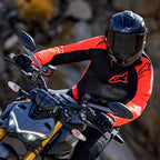Alpinestars Viper Air V4-jacka, Red Fluo och svart, bärs av en motorcykelförare som lutar sig in i en sväng på en sporthoj, svart integralhjälm och handskar, högpresterande racing- och sportutrustning