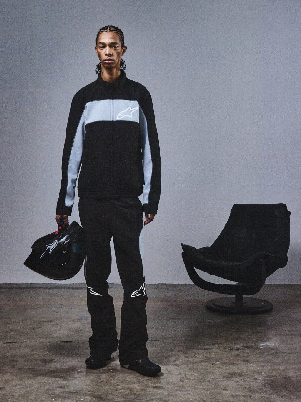 Alpinestars RSRV Track Jacket, svart och grå trackjacka med stjärnlogo, person håller svart hjälm, modern motorsport streetwear, minimalistisk design