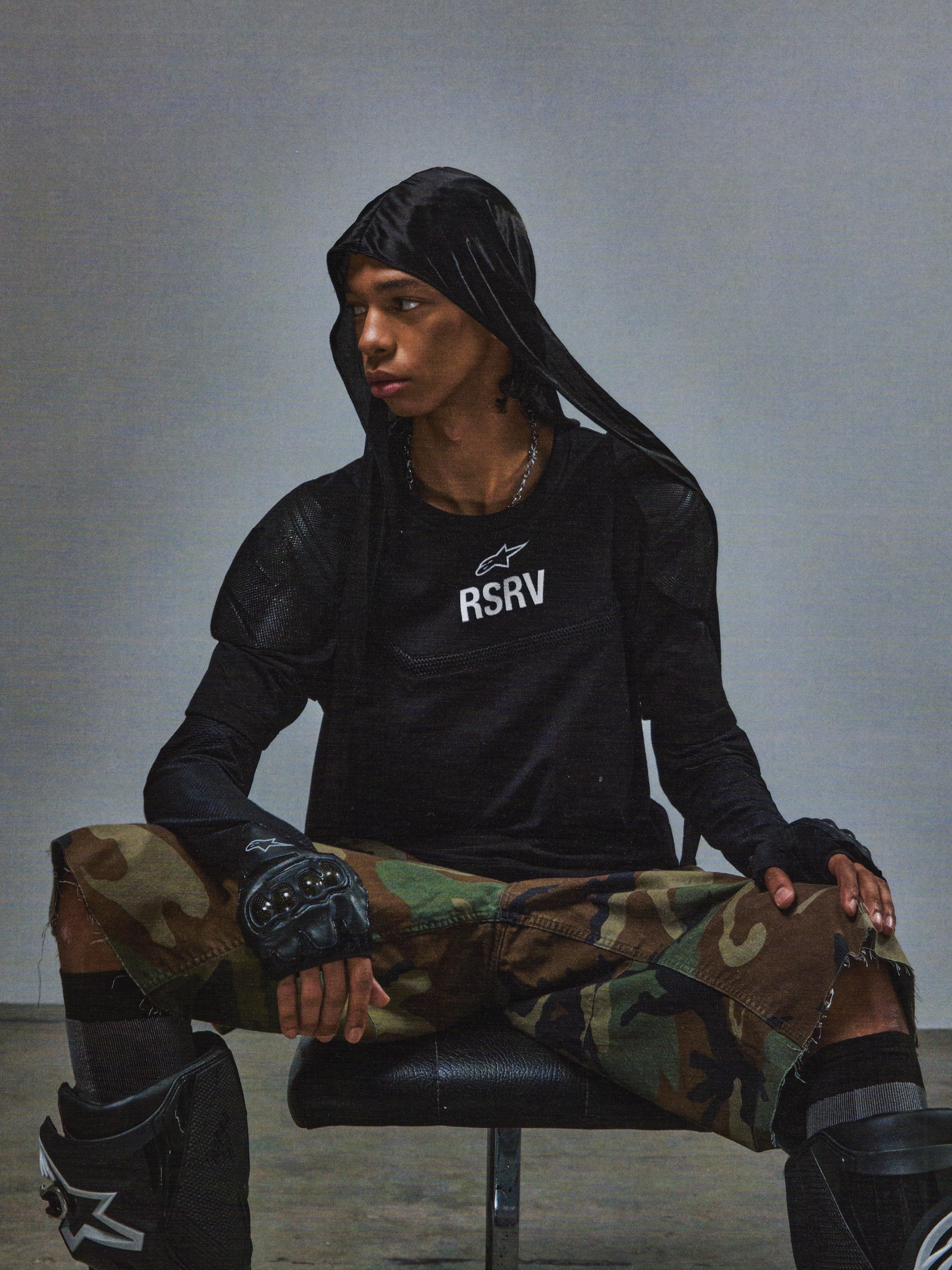 Alpinestars RSRV Nucleon SS Tee, svart t-shirt med vitt RSRV-tryck, person bär svart huvtröja, kamouflagebyxor i grönt och brunt, fingerløsa handskar med knogskydd, svarta knäskydd, urban taktisk stil