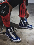Alpinestars RSRV Legacy Shoe, blå och vita höga sneakers, motorcykelskyddsutrustning, svarta skosnören, person som justerar skorna, sittande på stol, betongunderlag, blankt tyg och robust yta