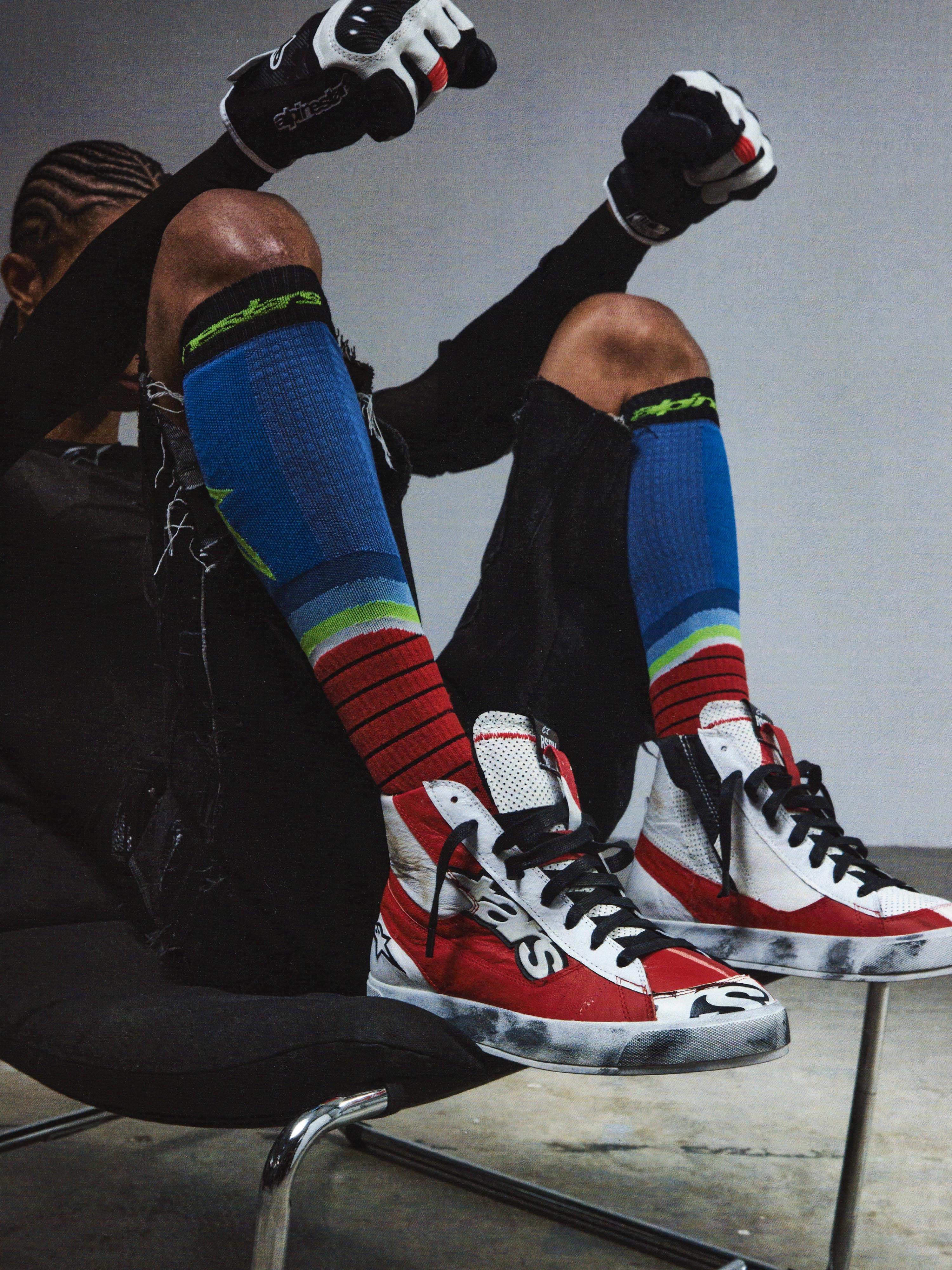 Alpinestars RSRV Legacy Shoe, röda och vita sneakers med svarta detaljer, premiumskor med logotyp, person bär färgglada strumpor och svarta handskar