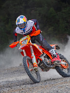Motocrossförare i action bärande Alpinestars Pro-Dura Jersey i svart, klarröd och vit, körandes en orange motocrosscykel på ett dammigt terrängspår, kombinerat med svarta byxor och röd-vita stövlar.