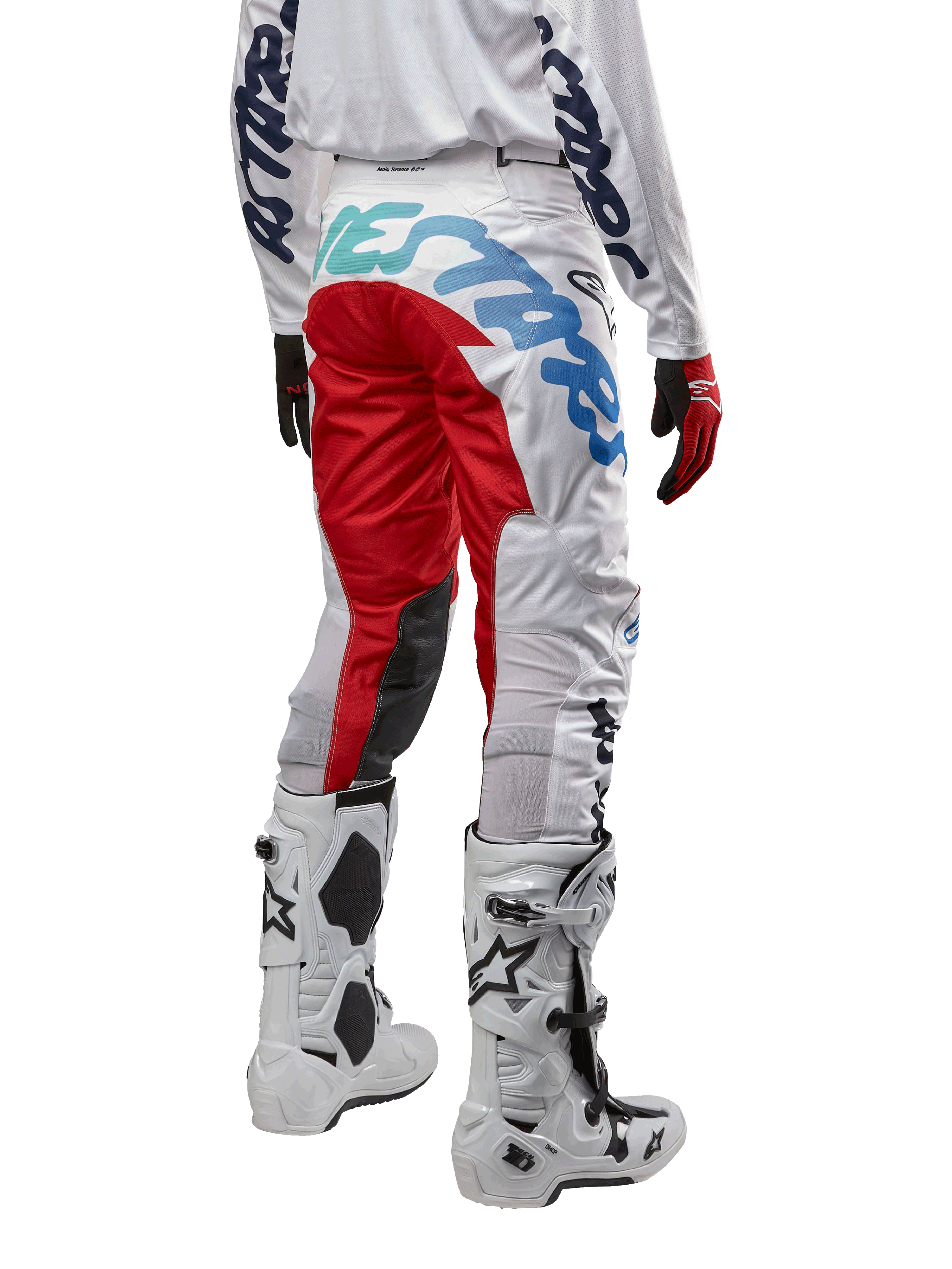 Alpinestars 2024 Racer Hana byxor, motocrossbyxor, vita flerfärgade med röda och blå detaljer, vy bakifrån som visar stor logotyp på baken, bärs med vita och svarta motocross-stövlar, designade för offroad-prestanda och hållbarhet