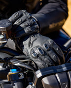 Alpinestars SP X 7-handskar, svarta motorcykelhandskar i perforerat läder med TPU-knogskydd och fingersliders, visas på en förares händer som greppar ett motorcykelstyre