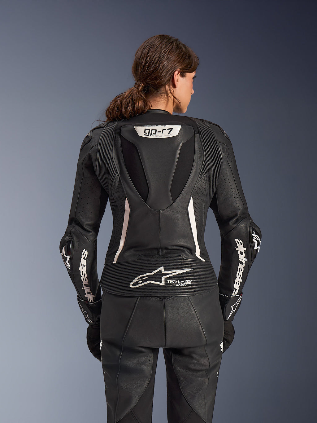 Alpinestars Stella GP-R7 2-delat läderställ, MC-ställ för damer, svart med vita detaljer, ryggvy som visar Supertech R10-aeropuckeln med GP-R7-logotyp, Tech-Air Ready-märkning på nedre ryggen, vit Alpinestars-text på ärmarna och dragspelspaneler i stretch för racingprestanda