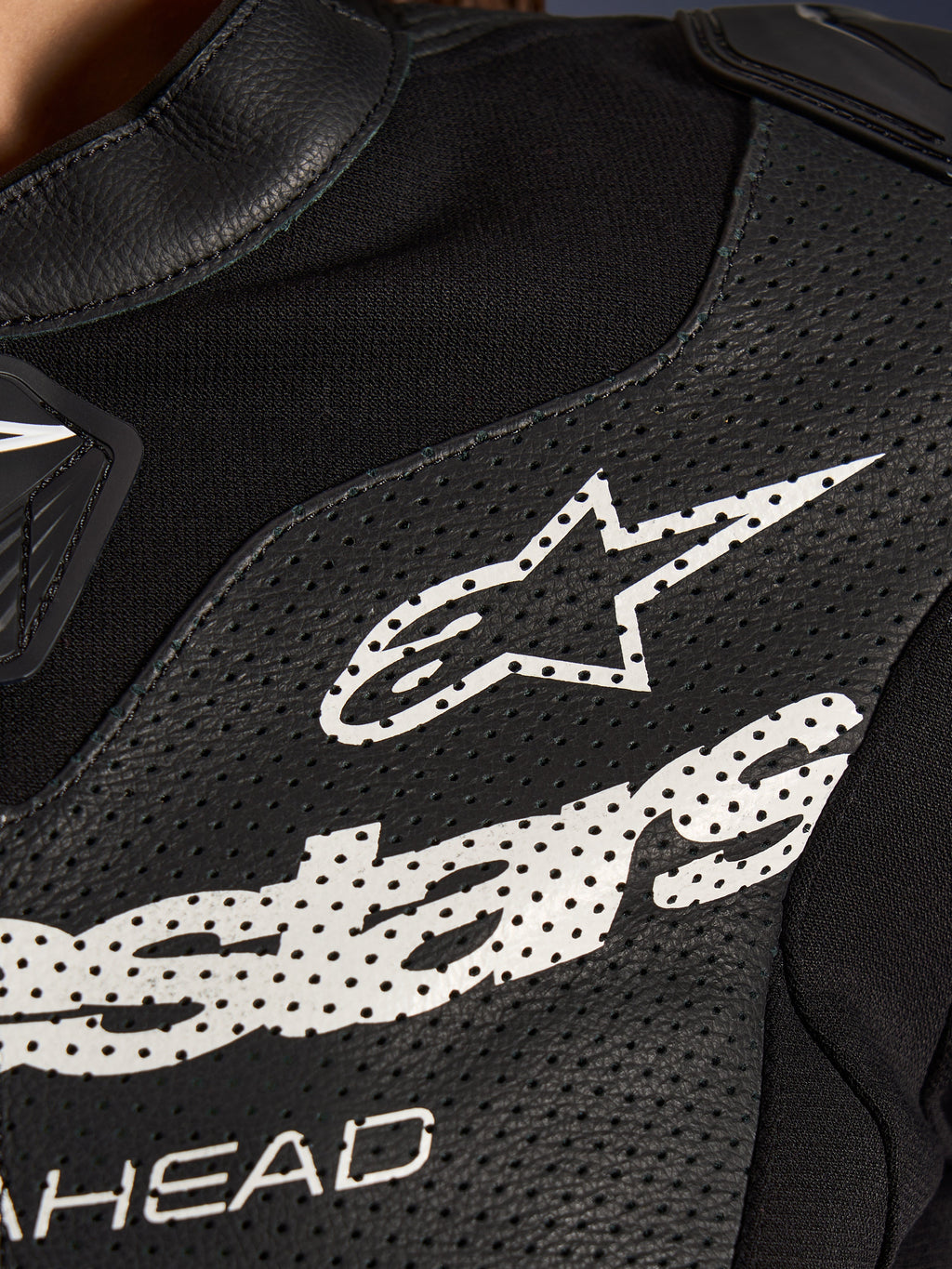Närbild av Alpinestars Stella GP-R7 2-delat läderställ i svart, med perforerade läderpaneler, en stor vit Alpinestars-logotyp på bröstet och ventilerande sektioner i stretchtyg.