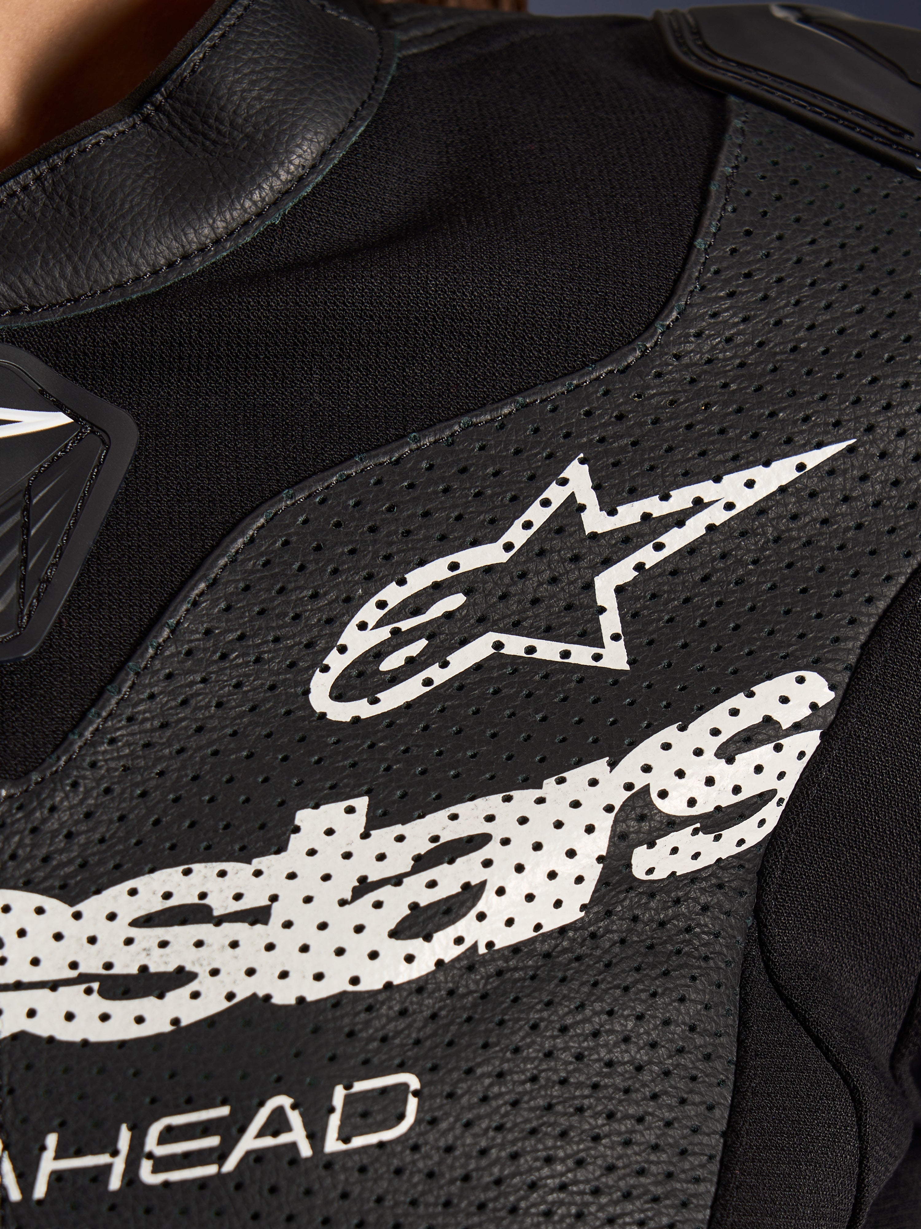 Närbild av Alpinestars Stella GP-R7 2-delat läderställ i svart, med perforerade läderpaneler, en stor vit Alpinestars-logotyp på bröstet och ventilerande sektioner i stretchtyg.