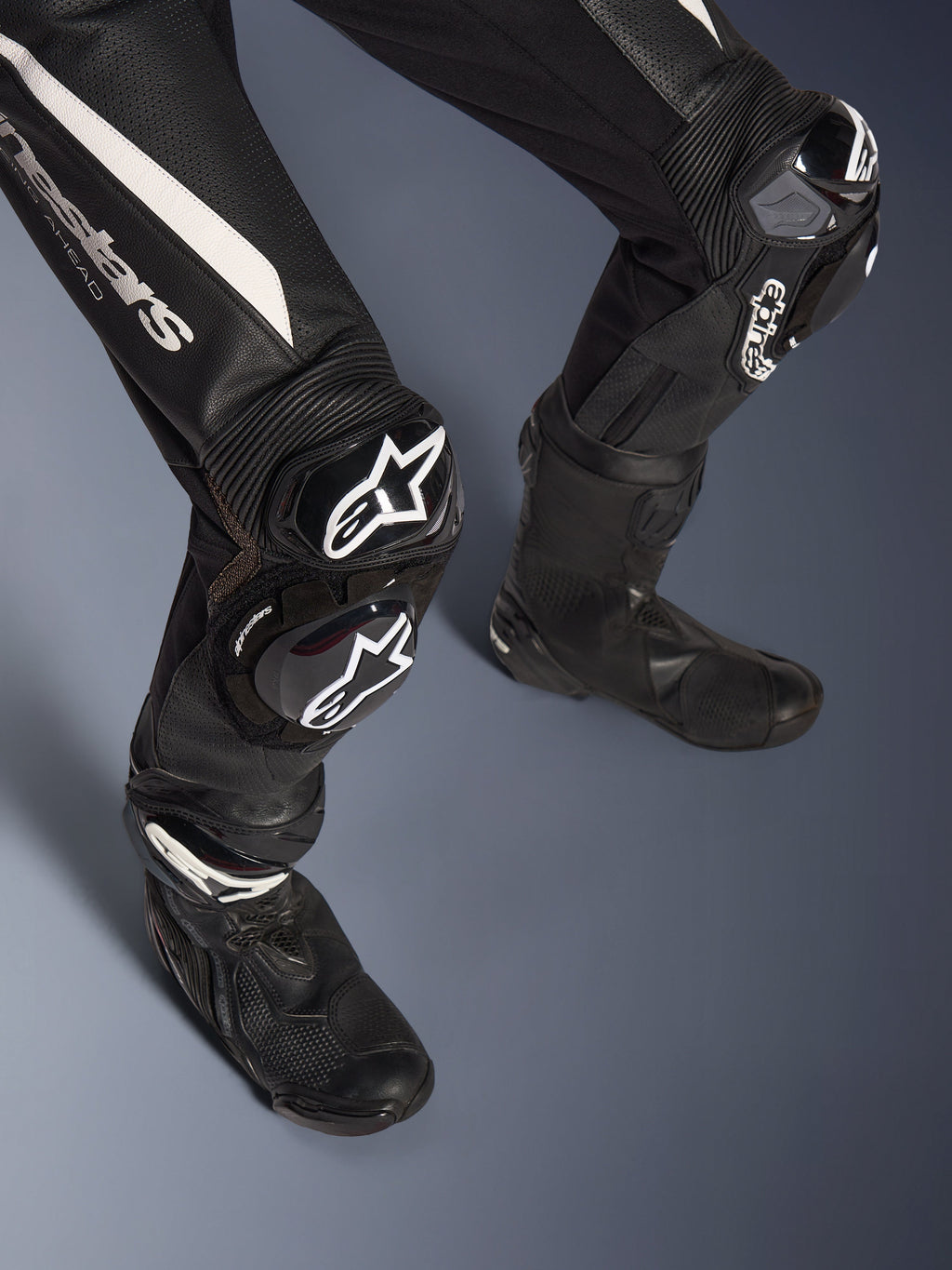 Detalj av benen på Alpinestars Stella GP-R7 2-delat läderställ för dam, svart med vita detaljer, med GP DFS RR knäskydd och sliders med Alpinestars logotyp, matchat med svarta racingstövlar, konstruerad för banprestanda