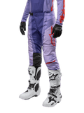 Alpinestars 2024 Techstar Ocuri byxor, motocrossbyxor i lila och stark orange, vita motorcykelstövlar med svarta detaljer, svarta handskar, atletisk racingdesign med ventilationshål och stretchmaterial för optimal rörelsefrihet vid terrängkörning.