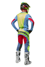 Motocrossförare sedd bakifrån iförd 2024 Techstar Ocuri-byxor och matchande tröja, ljusblå, fluorescerande gul och Red Berry, vita och svarta stövlar, svart hjälm med neondetaljer, koordinerad Alpinestars-utrustning för terrängkörning