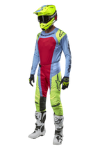 Motocrossförare klädd i Alpinestars 2024 Techstar Ocuri-byxor i ljusblått, neongult och rött, komplett racingutrustning med matchande tröja, neongul hjälm och vita stövlar, frontvy av tävlingsoutfit för terrängkörning.
