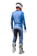 Motocrossförare sedd bakifrån bärande Alpinestars 2024 Techstar Pneuma-byxor i mörkblått och ljusblått, matchade med en blå tröja, vit hjälm, vita handskar och vita stövlar, med tydlig Alpinestars-profilering över sätet och ärmarna.