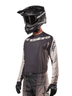 Alpinestars 2024 Techstar Pneuma Jersey, Motocross Racing Jersey, Dark Sand and Iron Dust Gray, long-sleeved performance top with laser-cut perforations and white branding, worn with matching pants and black helmet, athletic fit for off-road riding.