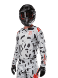 Alpinestars 2024 Techstar Rantera tröja, motocrosströja, Haze Gray Camo med svarta abstrakta mönster och röda accenter, långärmad design som bärs med matchande svart hjälm och handskar, teknisk racingutrustning för terrängkörning
