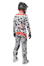 Motocrossförare sedd bakifrån iklädd Alpinestars 2024 Techstar Rantera-byxor, Haze Gray Camo med svarta fläckar och röda logotyper, matchande tröja, svart hjälm och vita stövlar, komplett outfit för terrängkörning