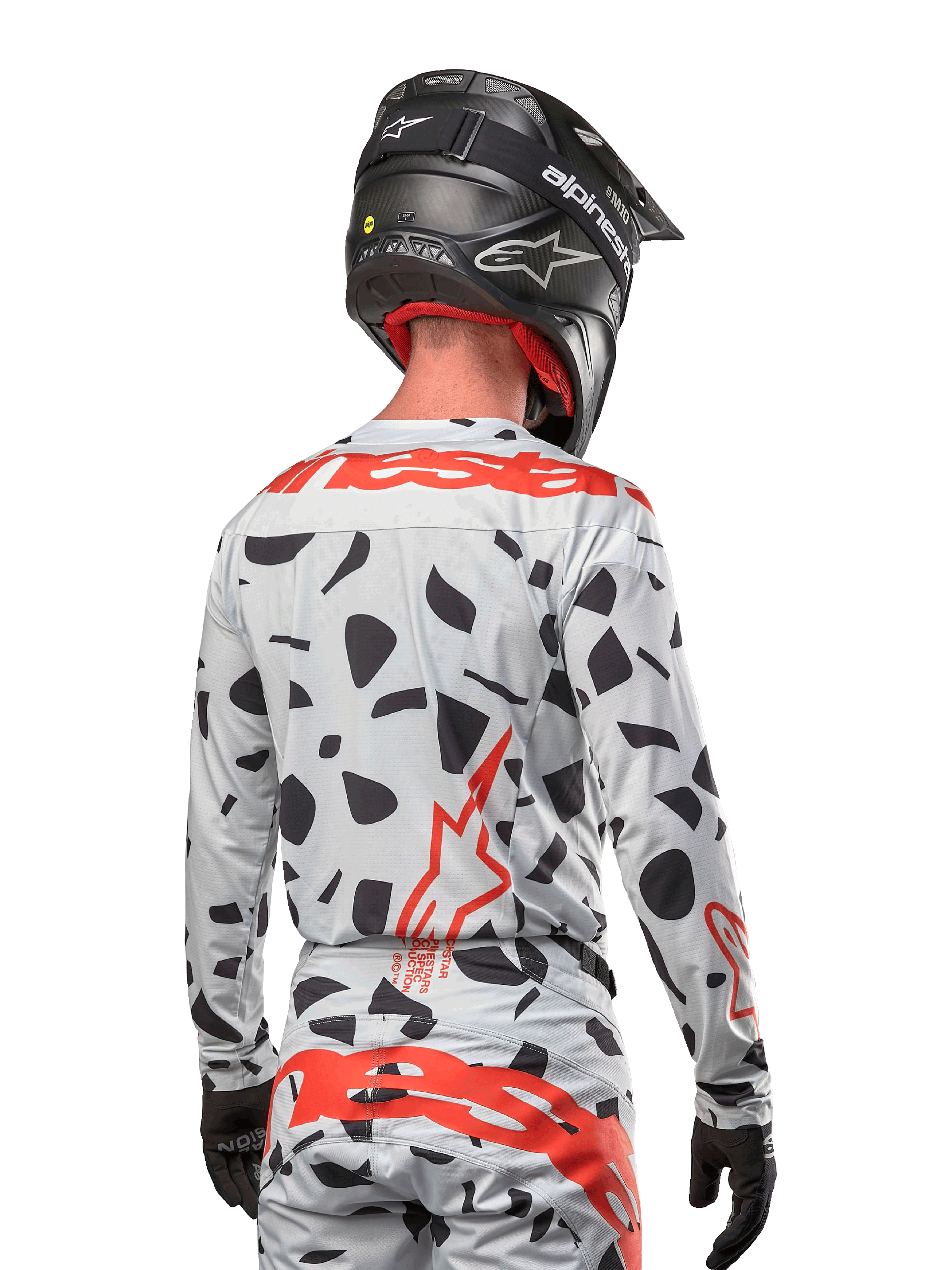 Motocrossförare sedd bakifrån i Alpinestars 2024 Techstar Rantera-tröja i Haze Gray Camo, med en ljusgrå bas med svarta grafiska fläckar och framträdande röda Alpinestars-logotyper på ryggen och axlarna, matchad med matchande byxor och en svart hjälm.