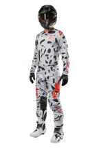 Alpinestars 2024 Techstar Rantera-byxor, motocrossbyxor, Haze Gray Camo, bärs med matchande tröja, svart hjälm samt vita och svarta stövlar, med svarta abstrakta mönster och röda detaljer, komplett utrustning för terrängkörning