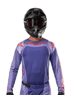 Alpinestars 2024 Techstar Ocuri-tröja, lila och starkt orange, bärs av en motocrossförare med svart hjälm och goggles, laserskurna perforeringar på bröstet, atletisk tävlingspassform och framträdande röd logotyp på axlar och bröst.