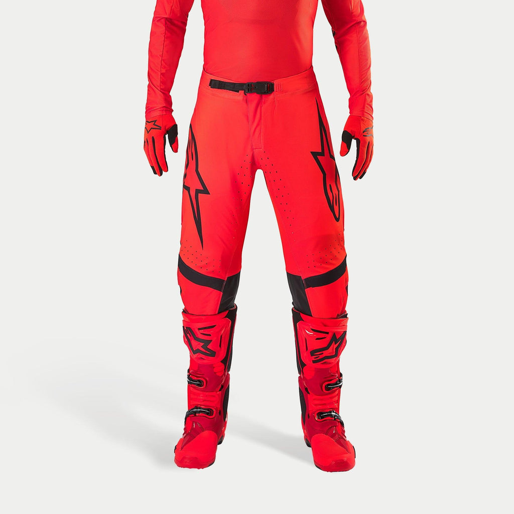 Alpinestars Supertech Ember LE byxor, motocrossbyxor, Red Fluo och klarröda med svarta detaljer, med framträdande svarta stjärnlogotyper på låren, svart midjespänne och knäpaneler, bärs med matchande röda stövlar och handskar för en koordinerad racingoutfit.