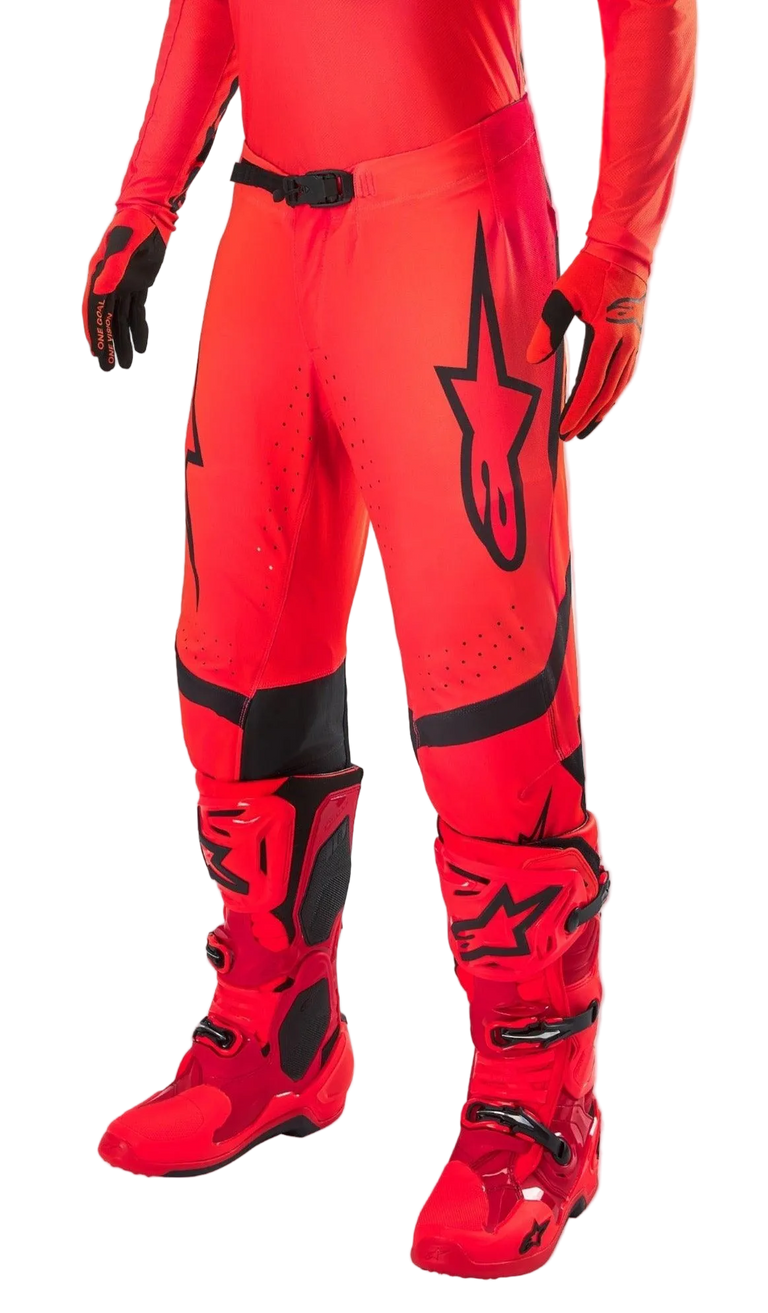 Alpinestars Supertech Ember LE Motocross Pants, Red Fluo and Bright Red with Black accents, worn with matching red racing boots and gloves, featuring a prominent black star logo on the leg, secure waist buckle, and perforated zones for ventilation.