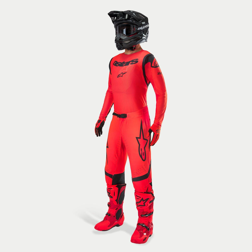 Motocrossförare i komplett racingutrustning, Supertech Ember LE-tröja och byxor i Red Fluo och svart, svart hjälm med goggles, matchande röda och svarta stövlar och handskar, professionell outfit för terrängkörning