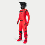 Motocrossförare i komplett racingutrustning, Supertech Ember LE-tröja och byxor i Red Fluo och svart, svart hjälm med goggles, matchande röda och svarta stövlar och handskar, professionell outfit för terrängkörning